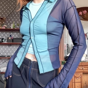 Blå meshskjorta med knappar - Mjuk och stretchig meshskjorta med knappar och krage. Den har en genomskinlig design och långa ärmar med slitsar.  Längd: 49cm Bredd: 42,5cm Ärm: 66cm