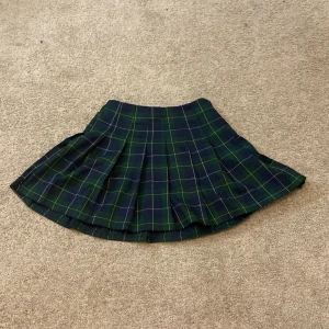 Rutig kjol från H&M - Snygg rutig kjol i blått och grönt från Divided. Kjolen har en klassisk plisserad design med dragkedja i sidan för enkel påklädning. Perfekt för en stilren look.