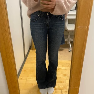 Blå bootcut jeans från Mudd - Snygga blå bootcut jeans från Mudd med klassisk femficksdesign och dekorativa sömmar på bakfickorna. Jeansen har en dragkedja och knapp framtill. 