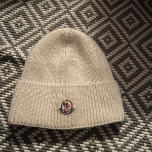 Vit stickad mössa från Moncler - Snygg vit stickad mössa från Moncler med ribbad kant och broderad logotyp framtill. Perfekt för kyliga dagar och ger en stilren look.