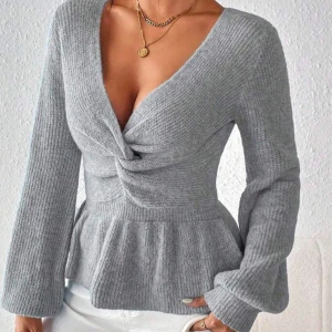 Grå ribbad tröja med knutdetalj - Snygg grå ribbad tröja med en unik knutdetalj framtill. Tröjan har långa ärmar och en peplum-effekt vid midjan som ger en smickrande silhuett. Perfekt för kyligare dagar. Använt 1 gång och säljer den då den inte kommer till användning och bara ligger i garderoben. Köp gärna!❤️  