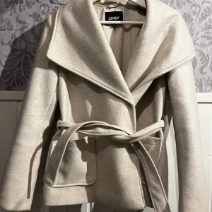 Beige kappa från ONLY - Snygg beige kappa från ONLY med knytbälte i midjan. Storlek xs väldigt fint skick. Nypris 559kr