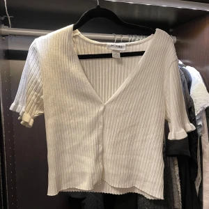 Vit ribbad kofta från Monki - Säljer en vit ribbad kofta från Monki med korta ärmar, knappar framtill & volanger på ärmarna! 