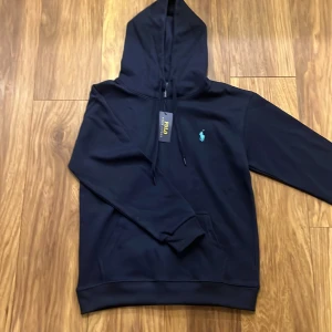 Mörkblå hoodie från Polo Ralph Lauren - Snygg mörkblå hoodie från Polo Ralph Lauren med det klassiska logotypbroderiet i ljusblått på bröstet. Tröjan är helt ny och sitter som en liten S eller stor XS. Säljer billigt eftersom den bara tar onödig plats
