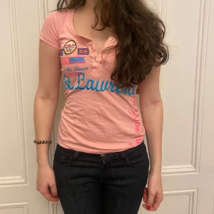 Rosa kortärmad topp med tryck - Säljer en rosa kortärmad topp med flera tryck och broderier i blått och rött. Toppen har en knappdetalj framtill och en djup v-ringning. Perfekt för sommaren!!!