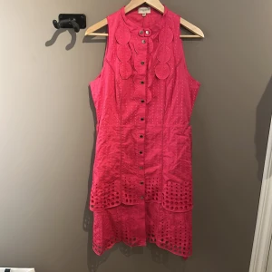 Rosa klänning från Karen Millen - Snygg rosa ärmlös klänning från Karen Millen med dekorativa cirkeldetaljer och knappar framtill. Klänningen har ett unikt mönster och en lätt volangkant nedtill. Perfekt för en somrig look!