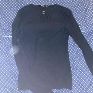 Svart ribbad tröja från BikBok - Snygg svart ribbad tröja från BikBok i storlek XS. Tröjan har en unik detalj med en ring vid halsen och långa ärmar. Perfekt för en stilren look.