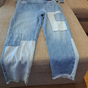 Blå jeansbyxdress med lappar - Säljer en cool blå jeansbyxdress (jumpsuit) med lappar i olika nyanser. Den har justerbara hängslen och flera fickor, vilket ger en avslappnad och trendig look. Perfekt för en casual dag ute eller en chill kväll med vänner. Passar bra med en enkel t-shirt under!