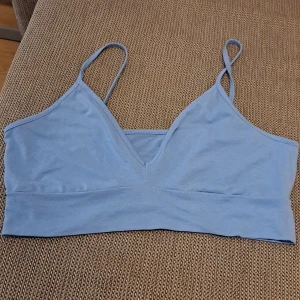 Ljusblå ärmlös topp - Säljer en superfin ljusblå topp med smala axelband och v-ringning. Perfekt för sommardagar eller som ett lager under en tröja. Toppen är i ett mjukt och bekvämt material.