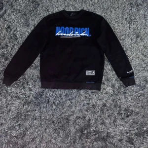 Svart sweatshirt från Hoodrich - Säljer en svart sweatshirt från Hoodrich med blå och vit text på framsidan. Tröjan har långa ärmar och en normal passform. Perfekt för en casual look eller streetwear-stil. Texten 'From Nothing to Something' finns tryckt på baksidan.