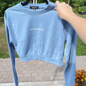 Croppad sweatshirt - En croppad blå sweatshirt från Missguided. Sann i storleken då den passar bra till mig som har S. Säljer den pga att den inte kommer till användning 💕💕  Använd max 3 gånger 💙  Längd: 39 cm Axel: 48 cm Byst: 91 cm