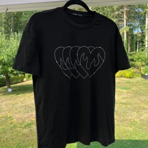 Oversized svart t-shirt - En svart oversized t-shirt med strass-detalj på bröstet. T-shirten är i storlek XS och är snyggt oversized till mig som har S.  Fint skick, använd max 5 gånger 💞  Längd: 66 cm Axel: 52 cm Byst: 106 cm