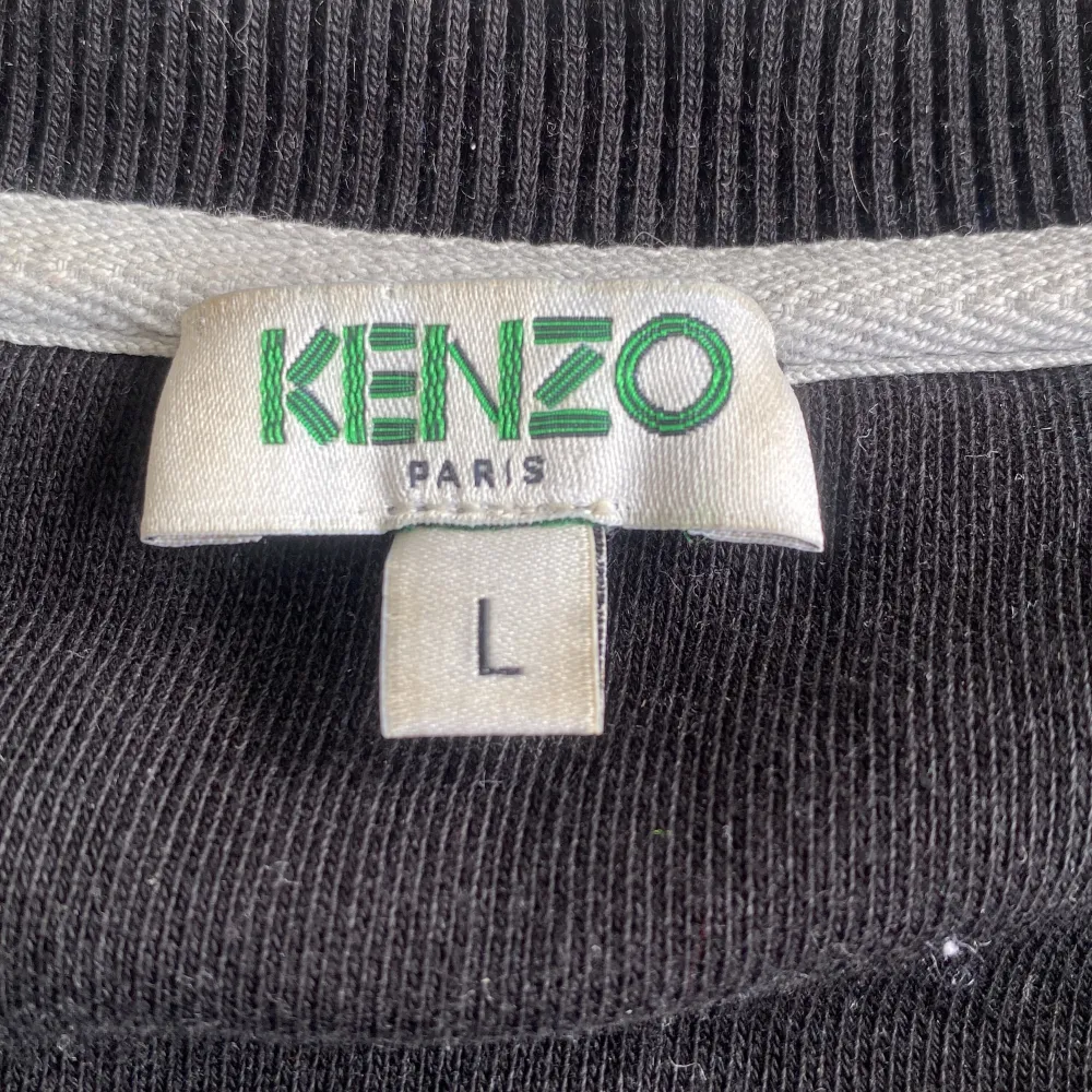 Säljer en helt ny svart sweatshirt från Kenzo med ett coolt broderi av en tiger i blått, gult och vitt på framsidan. Tröjan är långärmad och har en normal passform. Perfekt för både vardag och fest! . Tröjor & Koftor.