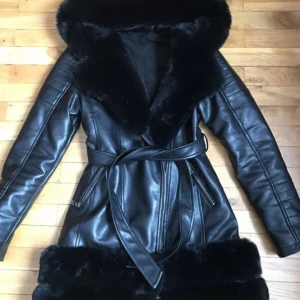 Svart skinnjacka med pälsdetaljer - Säljer en snygg svart skinnjacka med mjuka pälsdetaljer på kragen och ärmsluten. Jackan har en stilren design med ett bälte i midjan för en figursydd passform. Ps skärpen kommer inte med då jag tappat bort den. 