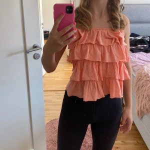 Persikofärgad volangtopp - Säljer en superfin persikofärgad topp med volanger. Den är ärmlös och har smala axelband, perfekt för sommaren. Toppen är luftig och har en söt, romantisk stil. Passar både till vardags och fest!