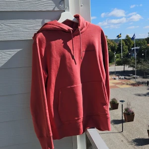 Röd hoodie från J.Lindeberg - Säljer en snygg röd hoodie från J.Lindeberg i storlek S. Den är perfekt för höst och vår med sin mjuka bomullskänsla. Hoodien har en klassisk design med en stor ficka fram och justerbar huva. Den är i nyskick och redo för nya äventyr!