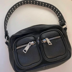 Svart axelväska från Noella - Snygg svart axelväska i syntet med två framfickor och dragkedjor från Noella