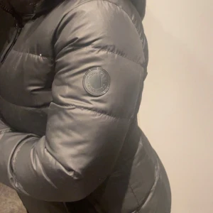 Svart dunjacka med pälshuva - Snygg svart dunjacka med dragkedja och en mysig pälshuva. Perfekt för kalla vinterdagar. Jackan har en normal passform och långa ärmar.