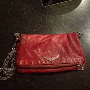 Röd axelväska med kedja - Säljer denna supersnygga och coola Zadig Voltaire-väska i äkta skinn.  Perfekt för att ge en cool färgklick till din outfit, och passar till allt. Denna specifika modell finns inte att köpa någonstans och därav mycket unik. (Är enligt mig den coolaste zadig väskan som finns/funnits). Köpte för runt 4000kr men säljer för 2500kr. Kvitto finns<3