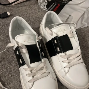 Valentino Garavani sneakers - Snygga vita Valentino Garavani sneakers med svarta detaljer och klassisk snörning. Skorna har en stilren design med märkets logotyp på sulan och insidan. Perfekta för en trendig look.