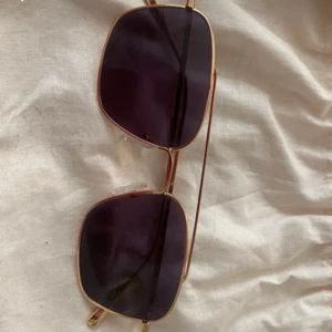 Solglasögon med guldtonad ram - Snygga solglasögon med fyrkantiga linser och en elegant guldtonad metallram. Perfekta för att ge en stilren touch till din outfit.