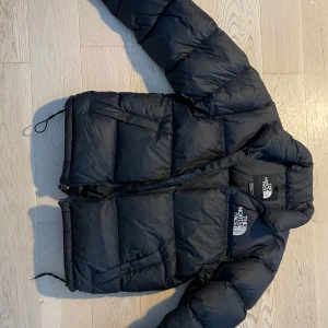 Svart dunjacka från The North Face - Säljer en svart pufferjacka från The North Face i storlek S. Jackan har en dragkedja framtill och är långärmad med elastiska ärmslut. Perfekt för kalla dagar med sin varma dunfyllning.