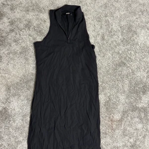 Svart ärmlös klänning - Snygg svart ärmlös klänning med dragkedja framtill. Perfekt för en stilren look. Klänningen har en enkel och elegant design som passar till många tillfällen.