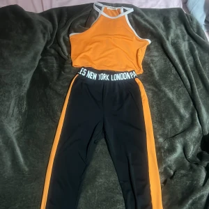 Orange och svart träningsset från Shein - Snyggt träningsset från Shein i orange och svart. Toppen är ärmlös med vita kanter och byxorna har en elastisk midja med text. Perfekt för träning eller en aktiv dag.