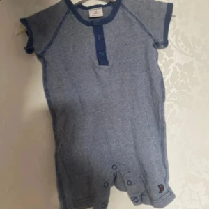 Blå kortärmad bodysuit från Polarn O. Pyret - Säljer en söt blå kortärmad bodysuit från Polarn O. Pyret. Den har mörkblå kantdetaljer och knappar framtill samt vid grenen för enkel påklädning. Perfekt för varma dagar!