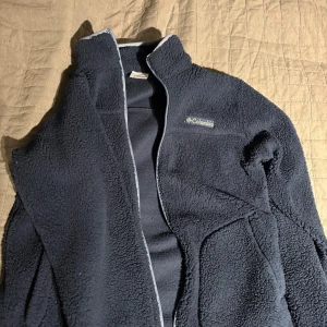 Mörkblå fleecejacka från Columbia - Säljer en mysig mörkblå fleecejacka från Columbia. Jackan har en dragkedja framtill och är perfekt för kyliga dagar. Den är långärmad och har en mjuk, värmande känsla.