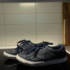 Glittriga Ralph lauren sneakers  - Snygga glittriga sneakers i mörkblått med snörning. Perfekta för att ge din outfit lite extra bling. De har en vit sula som kontrasterar snyggt mot det glittriga tyget. Det är blå Ralph Lauren skor, så gott som nya. Skorna är i storlek 39