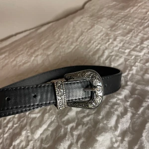 Svart bälte med detaljerad cowboy spänne från brandy Melville  - Snyggt svart bälte med ett detaljerat silverfärgat spänne. Bältet är från Brandy Melville och är ungefär 80cm långt