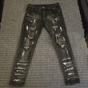Svarta jeans med slitningar och färgstänk - Säljer ett par svarta jeans med coola slitningar och unika vita och gula färgstänk. Perfekta för en edgy look. De har en slim passform och är midwaist. Passar perfekt för dig som vill sticka ut!