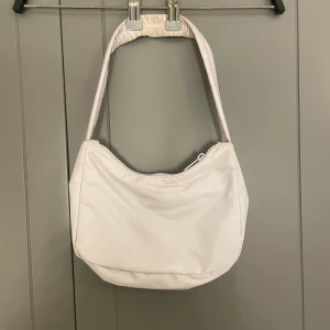 Ljuslila axelväska från Gina Tricot - Snygg ljuslila axelväska från Gina Tricot med dragkedja. Perfekt för att bära dina dagliga nödvändigheter. Enkel och stilren design som passar till många olika outfits.