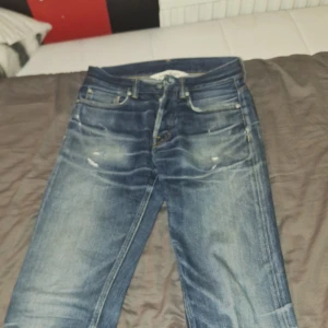 Blå jeans från Our Legacy slim/straight - Snygga blå jeans från Our Legacy med en klassisk femficksdesign. Nypris :4000.       De har en knappgylf och lätt slitna detaljer för en trendig look. Med slittna knappar.