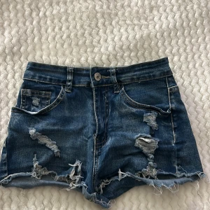 Blå jeansshorts från Shein - Snygga blå jeansshorts från Shein med slitna detaljer och fransig kant. Perfekta för en avslappnad stil. De har en knapp och dragkedja framtill samt klassiska fem fickor.