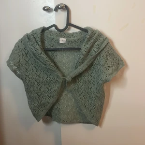 Grön stickad bolerotopp - Säljer en söt grön stickad bolerotopp med korta ärmar och ett fint spetsmönster. Perfekt för att lägga till en extra touch till din outfit. 