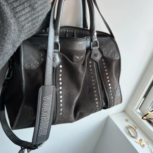 Svart handväska från Zadig & Voltaire - Snygg svart handväska från Zadig & Voltaire i skinn med coola nitar och dragkedja. Väskan har ett justerbart axelband med märkets logga och praktiska handtag. 🩷🩷.super fin, säljs inte längre. Nypris 7500kr