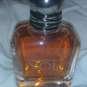 Stronger With You Intensely Parfym byter - Säljer en elegant parfymflaska från Emporio Armani, Stronger With You Intensely. Flaskan har en stilren design med en djup bärnstensfärgad vätska och en metallisk kork. Perfekt för den som vill ha en intensiv och långvarig doft.
