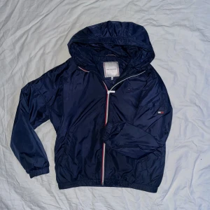 Tommy figer windbreaker - En Tommy hilfiger windbreaker. Nästan ny andvänd 2-3 gånger. Storlek 164. Den är också cropped längst nere.