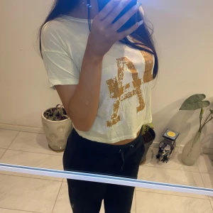 Vit t-shirt med guldtryck - Snygg vit t-shirt med ett stort guldtryck av bokstäverna 'LA' på framsidan. Perfekt för en avslappnad stil. Kortärmad och i en skön bomullsmix.