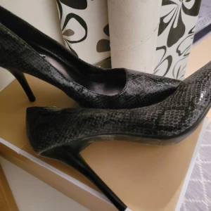 Svarta pumps med ormskinnsmönster - Eleganta svarta pumps med ormskinnsmönster och hög klack. Perfekta för en stilfull look.