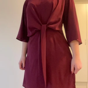Vinröd klänning med knytband - Elegant vinröd klänning med knytband i midjan och trekvartsärmar.