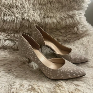 Beige pumps med glittriga detaljer från Catwalk - Eleganta beige pumps från Catwalk med spetsig tå och klack. Skorna är dekorerade med glittriga detaljer som ger en lyxig känsla. Perfekta för speciella tillfällen.