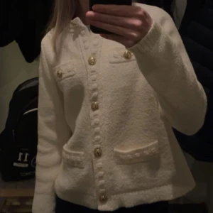 Vit kofta från H&M - Säljer en vit kofta från H&M med dekorativa guldknappar. Koftan har långa ärmar och två fickor framtill. Nypris är runt 499kr. 