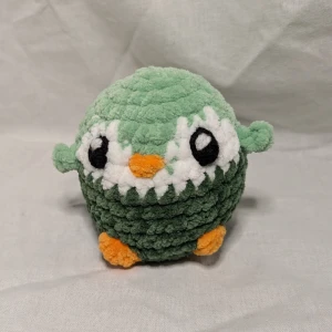 Grön och vit pingvin - Söt och mjuk virkad pingvinfigur i blått och vitt med orange detaljer. Perfekt som dekoration eller leksak. Den är gjord av 100% polyester. Höjd: 9 cm, bred: 8 cm
