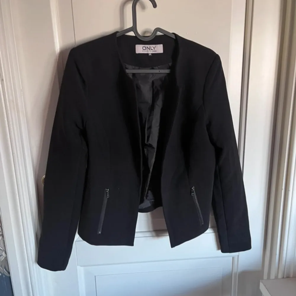 Snygg svart kavaj från ONLY i storlek 34. Kavajen har en stilren design med dragkedjor framtill och långa ärmar. Perfekt för en chic och elegant look.. Puvut & Bleiserit.