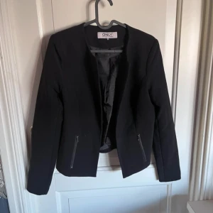 Svart kavaj från ONLY - Snygg svart kavaj från ONLY i storlek 34. Kavajen har en stilren design med dragkedjor framtill och långa ärmar. Perfekt för en chic och elegant look.