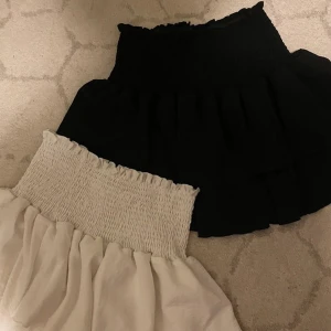 Svart och vit kortkjol - Två korta kjolar i svart och vit färg. Den svarta kjolen har en enkel design medan den vita har en elastisk, rynkad midja för extra komfort. Perfekta för en stilren look. Båda för 50kr och 1 för 20