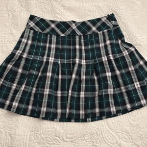 Rutig kjol från Lindex - Snygg rutig kjol från Lindex i grönt, svart och vitt. Kjolen har en dragkedja i sidan och är tillverkad av 65% polyester och 35% viskos. Längden är ungefär vid mitten låren!